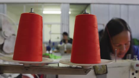 Mixed-race-woman-using-sewing-machine-in-factory