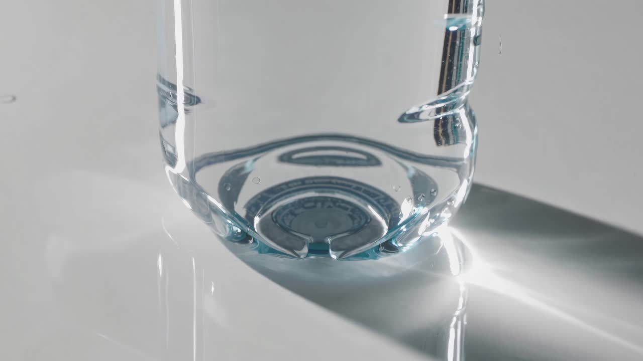 Close-up video shot of a clear water bottle on a reflective surface, capturing light refractions