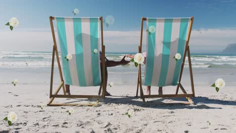 animación de flores blancas sobre una pareja diversa en sillas de sol con las manos en la playa