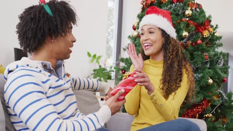 Video-of-happy-diverse-couple-exchanging-christmas-gift-and-embracing-at-home