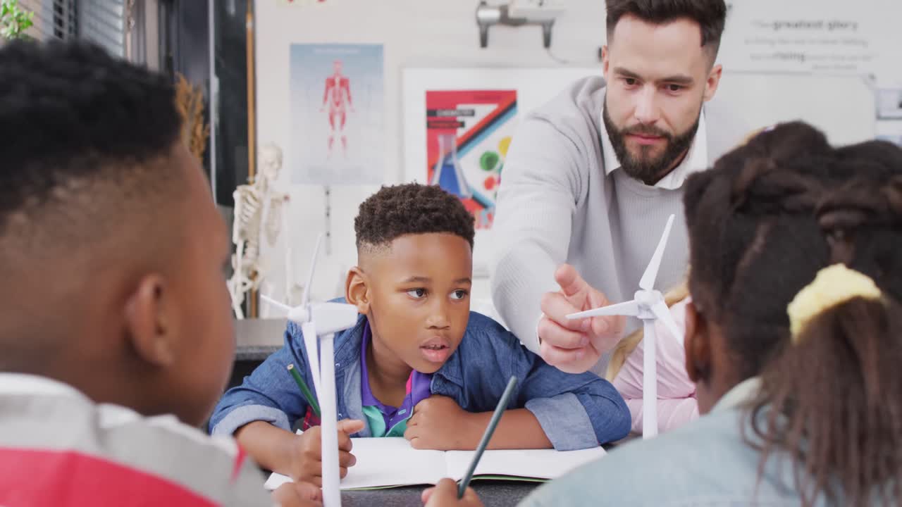 un maestro masculino diverso y escolares felices estudiando turbinas eólicas en el aula escolar