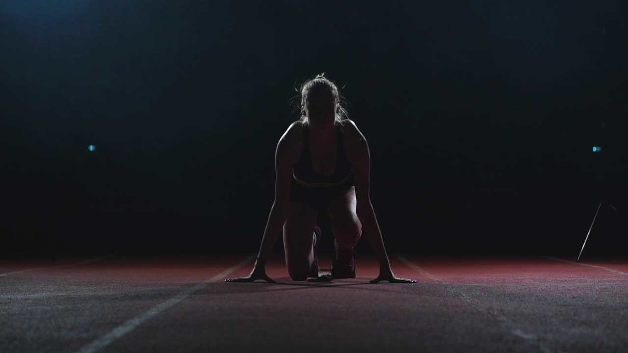 atleta femenina en un fondo oscuro se está preparando para correr el sprint de cross-country desde las almohadillas en la cinta de correr en un fondo oscuro