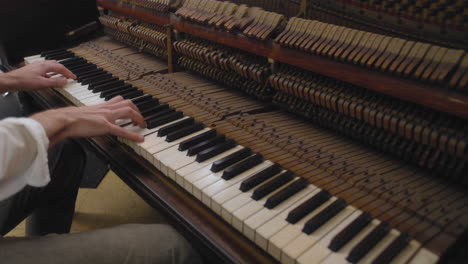 a man playing an upright piano with the hammer rail showing