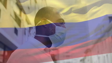 Animación-De-La-Bandera-De-Columbia-Ondeando-Sobre-Un-Hombre-Afroamericano-Con-Mascarilla-En-La-Calle-De-La-Ciudad