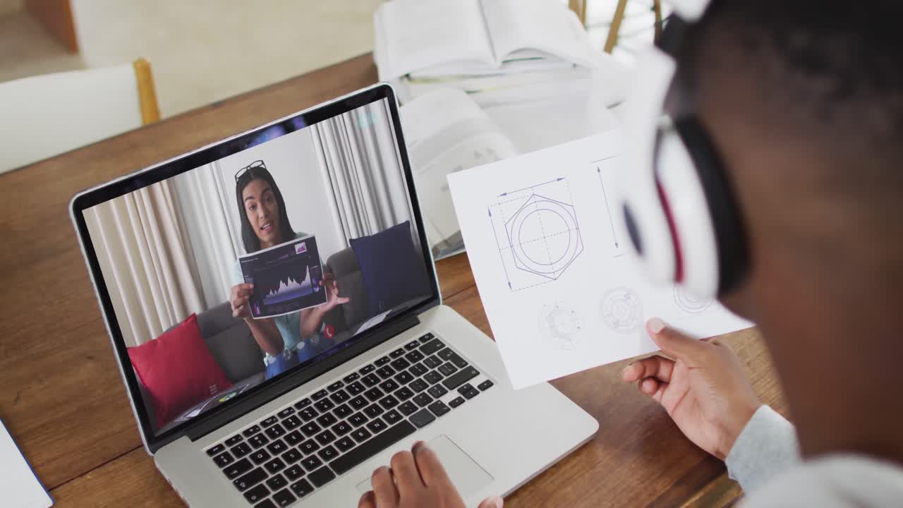 estudiante universitario afroamericano que sostiene notas mientras hace una videollamada en una computadora portátil en casa