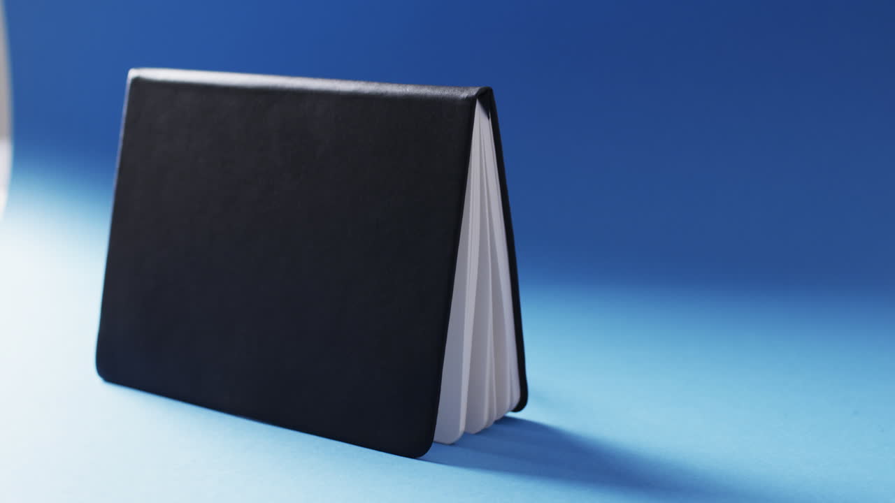 Close up of open black book standing horizontal with copy space on blue background in slow motion