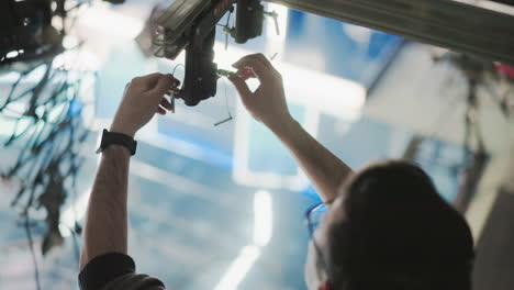 technician handling lighting rigging system, adjusting control unit with tools, focusing on fine adjustments in professional studio setting, preparing for production setup, ensuring precise alignment
