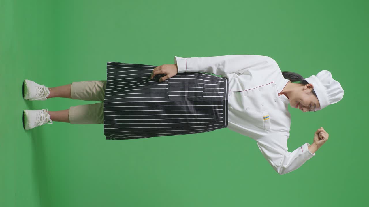 Full Body Of Asian Woman Chef Smiling And Flexing Her Bicep While Standing In The Green Screen Background Studio