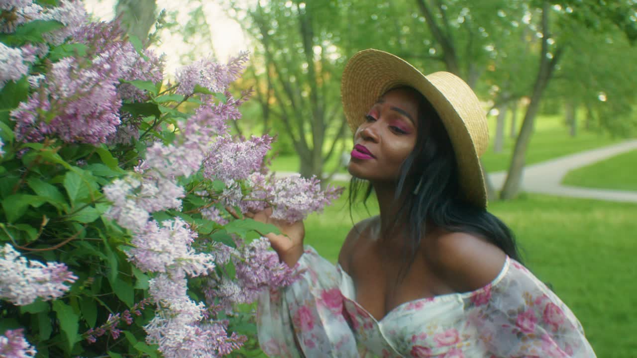 Femme noire sentant des lilas, souriante, avec contact visuel