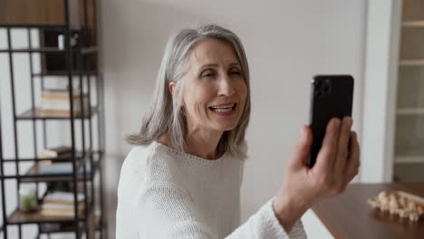 happy senior woman on a video call, while her friends wave at the camera while laughing and cooking