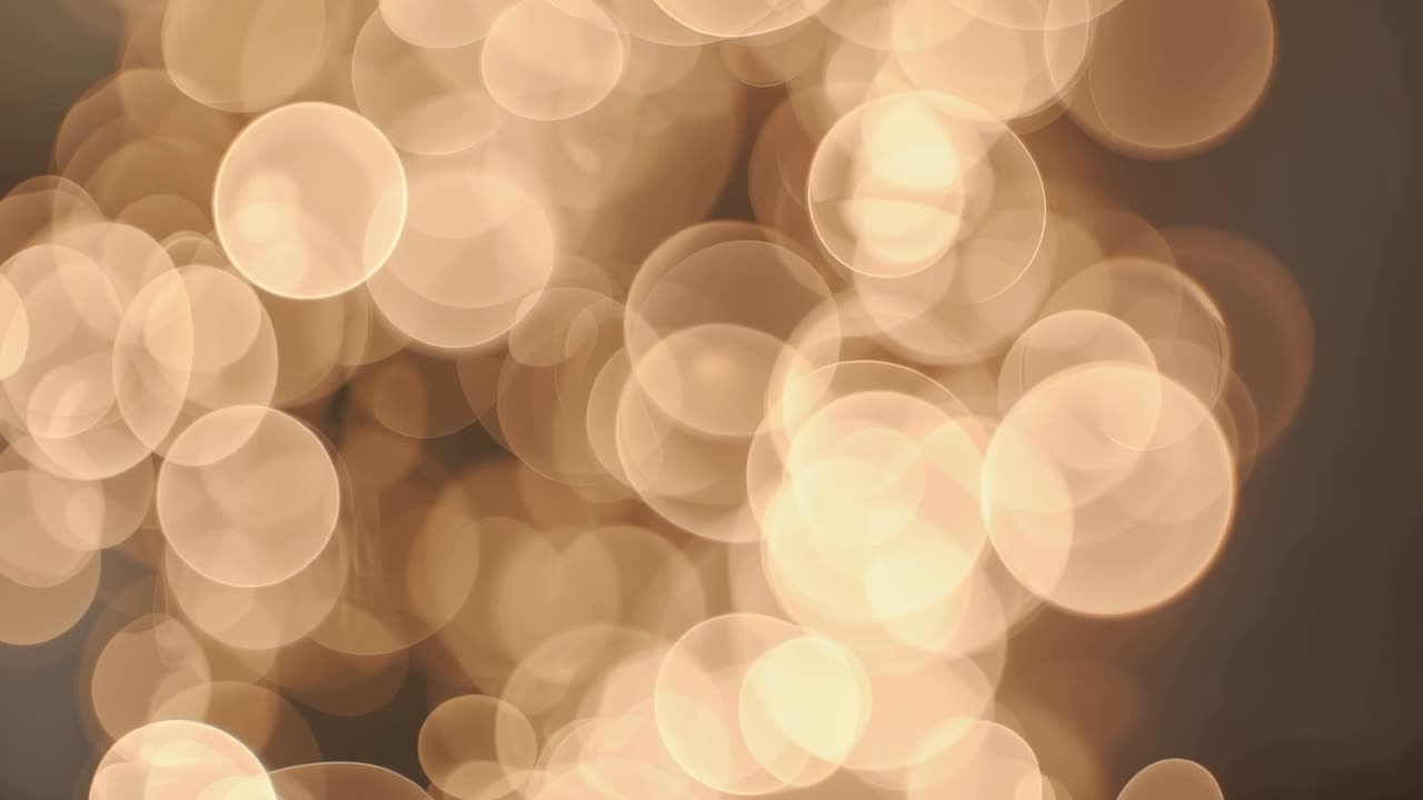 Shifting lens focus causing warm golden bokeh clusters drifting in dim room, creating warmth