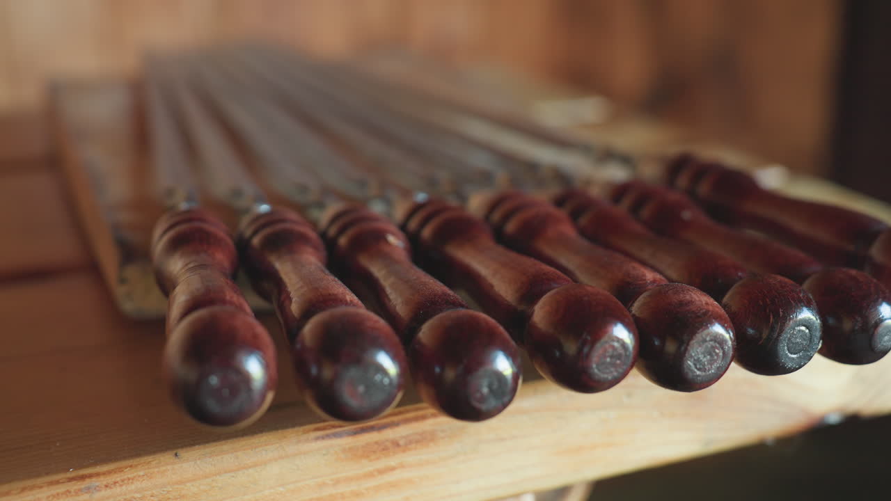 Close up of neatly arranged polished wooden skewers with dark glossy handles resting on rustic table under soft ambient light in cozy wooden interior setting perfect for barbecue preparation