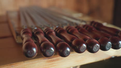 close up of neatly arranged polished wooden skewers with dark glossy handles resting on rustic table under soft ambient light in cozy wooden interior setting perfect for barbecue preparation
