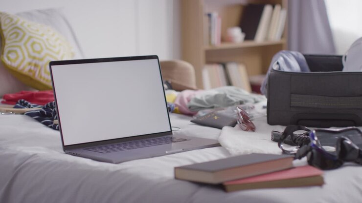 Laptop con schermo vuoto e valigia aperta sul letto a casa, in preparazione per le vacanze estive.