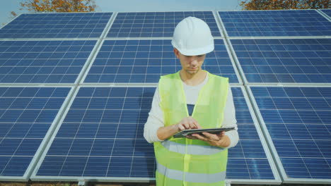 Junger-Ingenieur,-Der-Mit-Einem-Tablet-Vor-Dem-Hintergrund-Eines-Bodengestützten-Solarkraftwerks-Arbeitet-Working