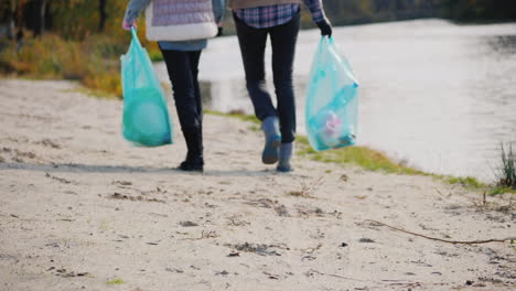 woman volunteer with a child walk along the lake carry packages with garbage