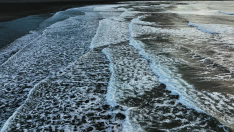 Drone-shot-tilting-over-waves-at-the-Stokksnes-beach,-toward-the-Vestrahorn-peak-in-Iceland