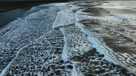 drone shot tilting over waves at the stokksnes beach, toward the vestrahorn peak in iceland