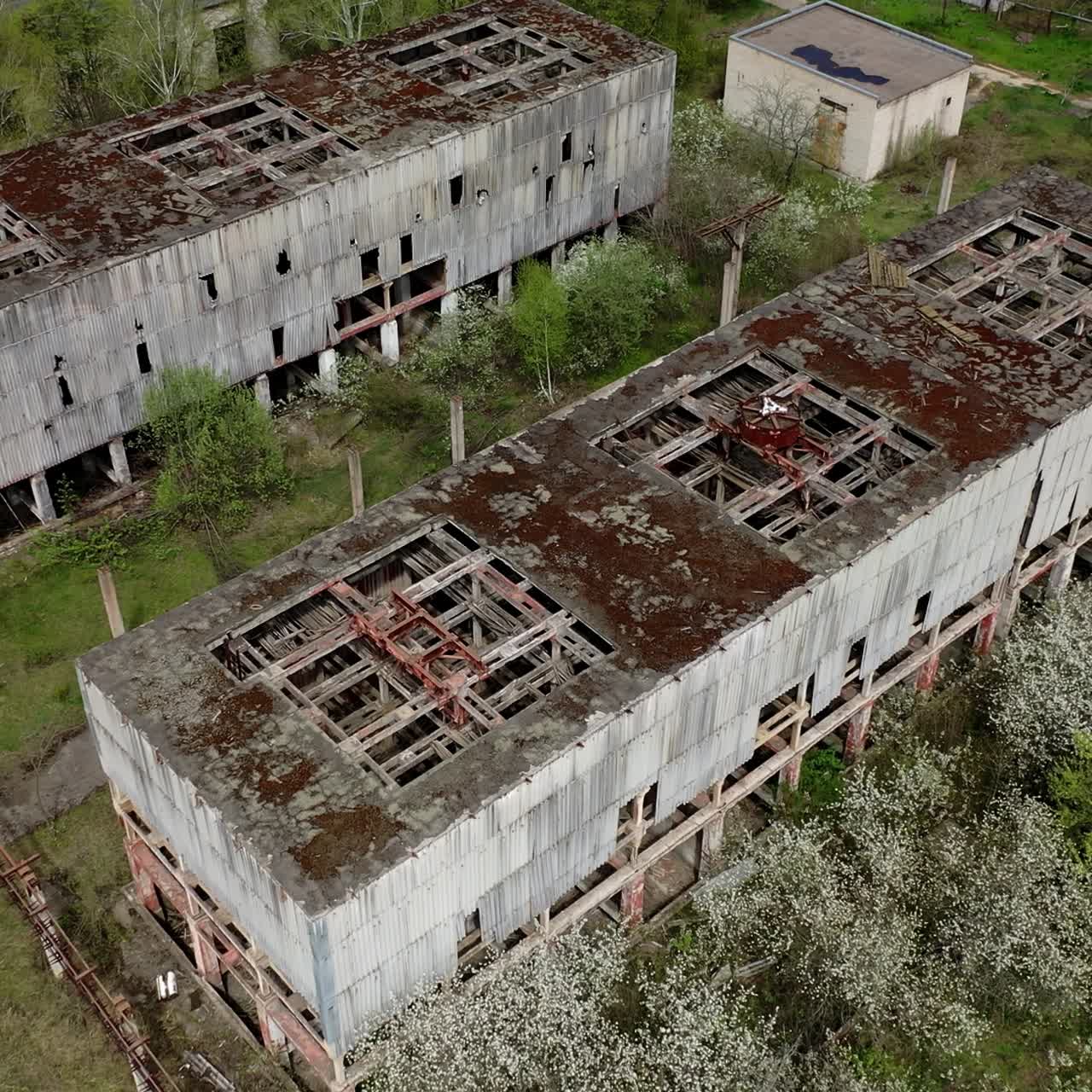 Destroyed factory buildings with holes in roofs. Old abandoned industrial plant. Ruined manufacturing on green nature background. View from above