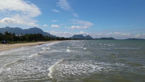 sliding to the right aerial footage revealing the beach, waves going to the shore, beach front and the horizon