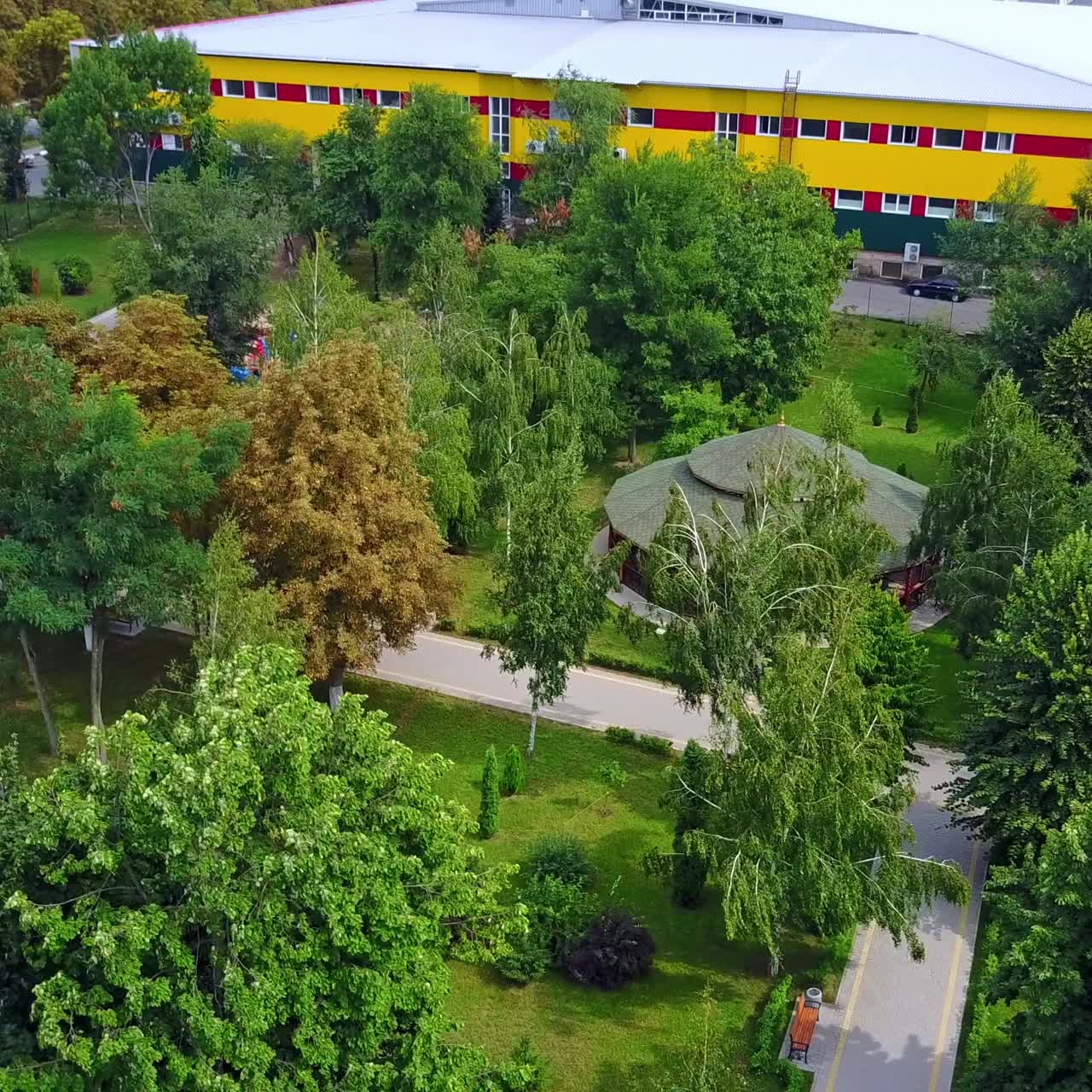Strong wind waving the trees in the city park. Two-storied yellow building at backdrop. Top view