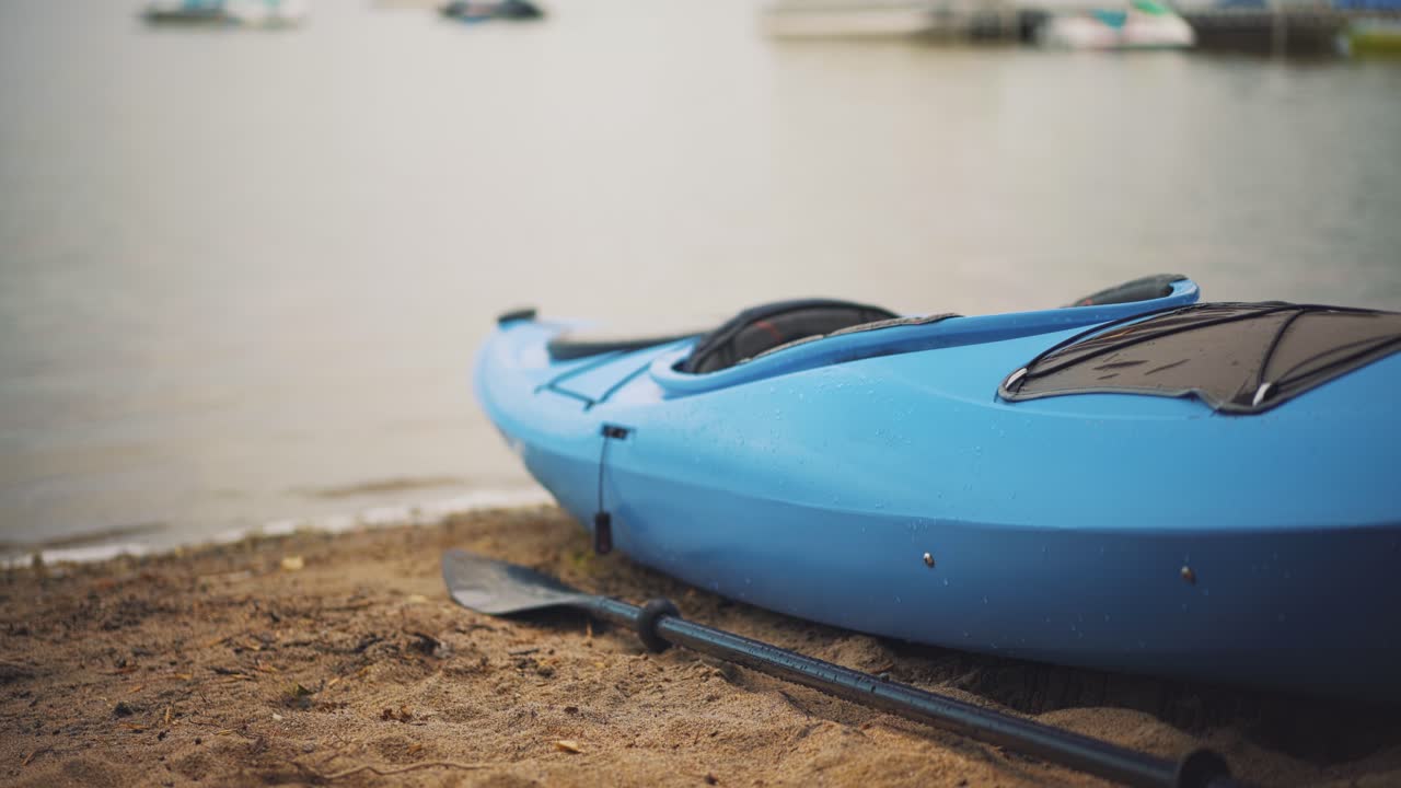 kayak y remo vacíos se sientan varado en la orilla de la playa de arena con olas tranquilas del lago en la distancia prores 4k