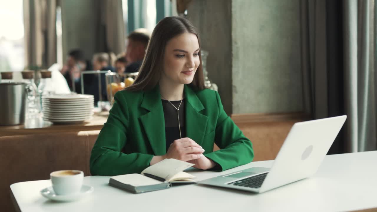charming woman in a green blazer starts a video call conversation using a laptop and holding a notebook