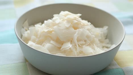 Slice-of-fresh-coconut-flakes-in-a-bowl-on-a-table-cloth-,