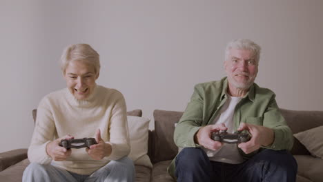 happy senior man and woman playing video game sitting on sofa at home