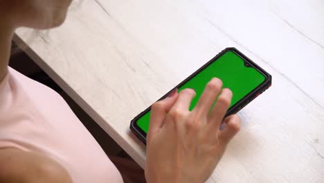 una chica durante una manicura usa un teléfono inteligente con una pantalla verde. servicio de manicura hecho a sí mismo. la manicurista pinta las uñas con gel polaco rosado. uñas rojas manicuradas. aplicación de esmalte de uñas.