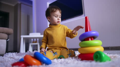 lovely caucasian toddler assembling the toy pyramid. cute baby boy playing peacefully at home.