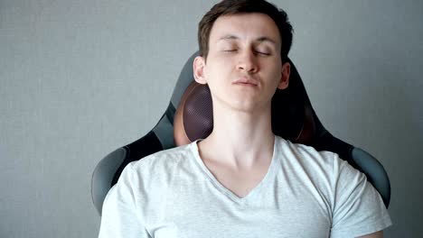 young man is sitting on the armchair with electric massage pillow