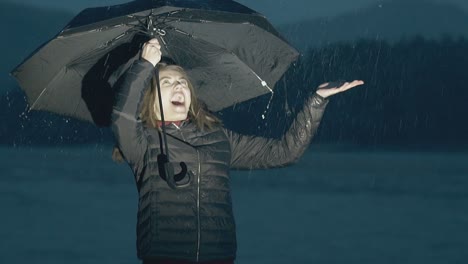 La-Mujer-Disfruta-Del-Clima-Lluvioso-Cerca-Del-Río-En-Cámara-Lenta-Por-La-Noche