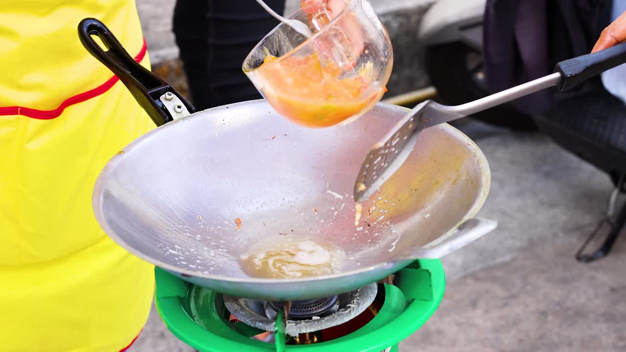 A person prepares an omelet in a wok on a portable stove, highlighting vibrant colors and dynamic cooking action