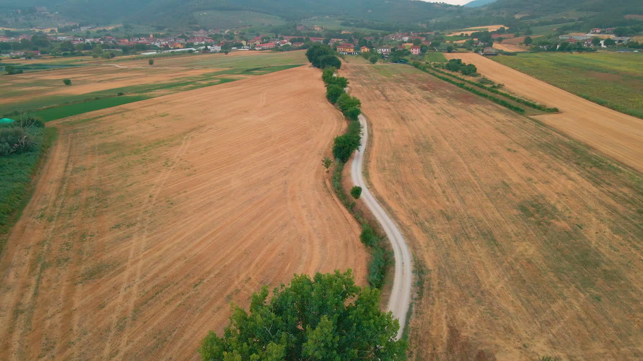 camino de tierra entre los campos, el pueblo y las montañas al fondo en magione, umbría, italia - toma aérea