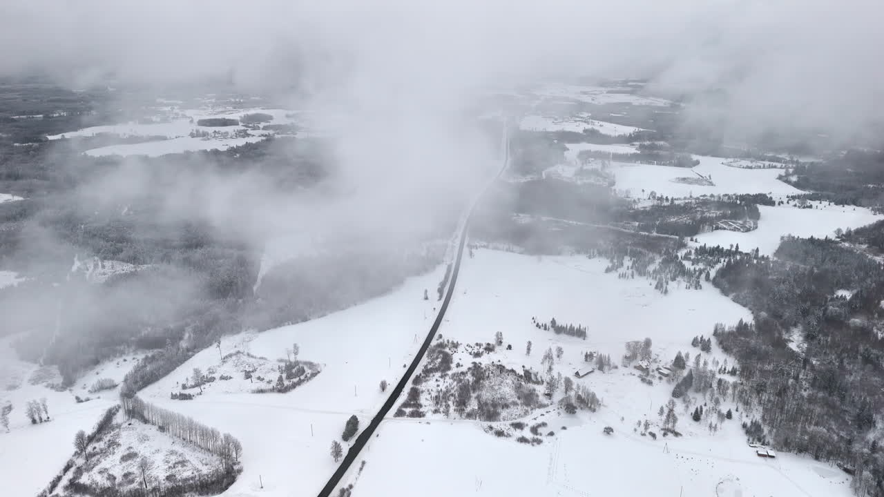 High drone shot with camera panning over a snowy landscape, with moving clouds passing in front of the view and a road crossing the scene