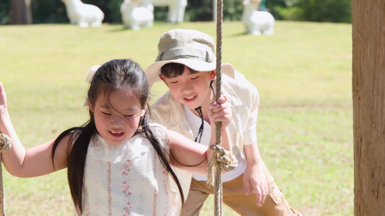 明るい日差しが降り注ぐ日当たりの良い公園で、ブランコに乗って一緒に遊ぶ幸せそうなタイのきょうだい。