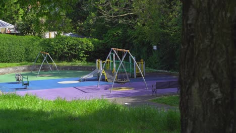 empty playground through fence no children or kids green grass swing and climbing frame.