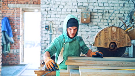 man in protective gloves and working clothes taking measures on the plant. worker is measuring stone slabs with the roulette indoors.