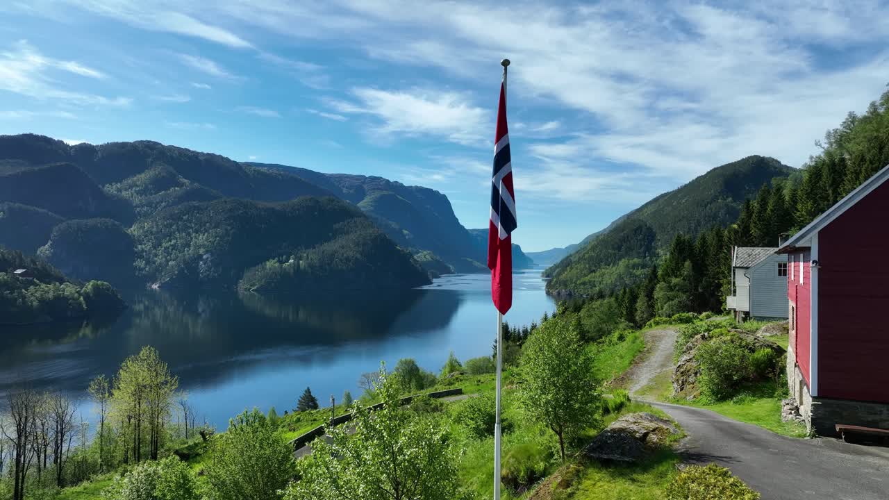Norwegian flag waves beside red barn above Veafjord fjord in stunning rural landscape. Summer scenery