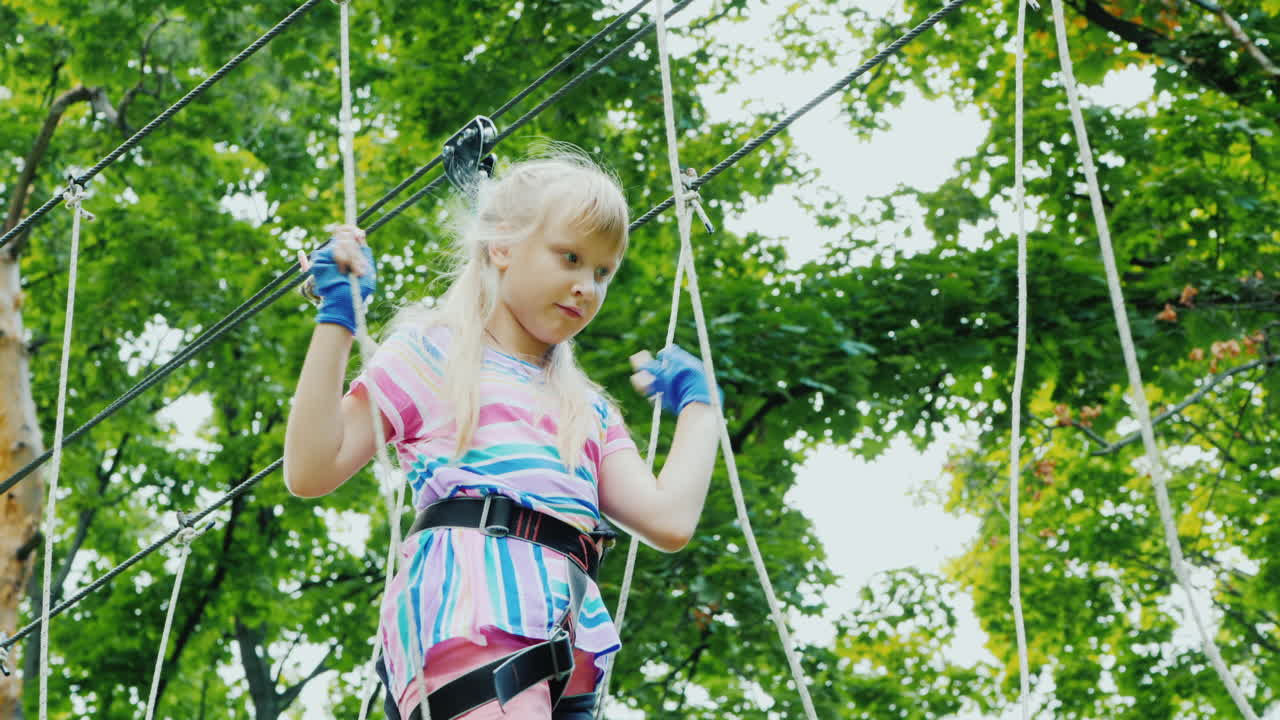 la vista trasera de una chica valiente se mueve a lo largo de las cuerdas entre los árboles usa una cuerda de seguridad