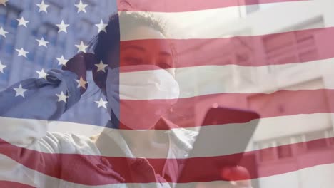 bandera estadounidense ondeando contra mujer asiática con máscara facial usando teléfono inteligente en la calle