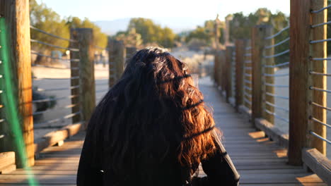 A-shot-from-behind-a-beautiful-girl-with-black-hair-sitting-down-and-practicing-meditation-and-mindfulness-in-the-desert-at-sunset