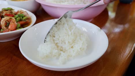 a fork fluffs white rice in a ceramic bowl.