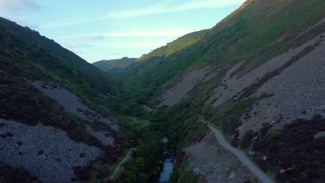 fast moving aerial heading up river with hiking paths on each side at sunrise with sunlight on top of valley. natural bird's eye view. drone footage