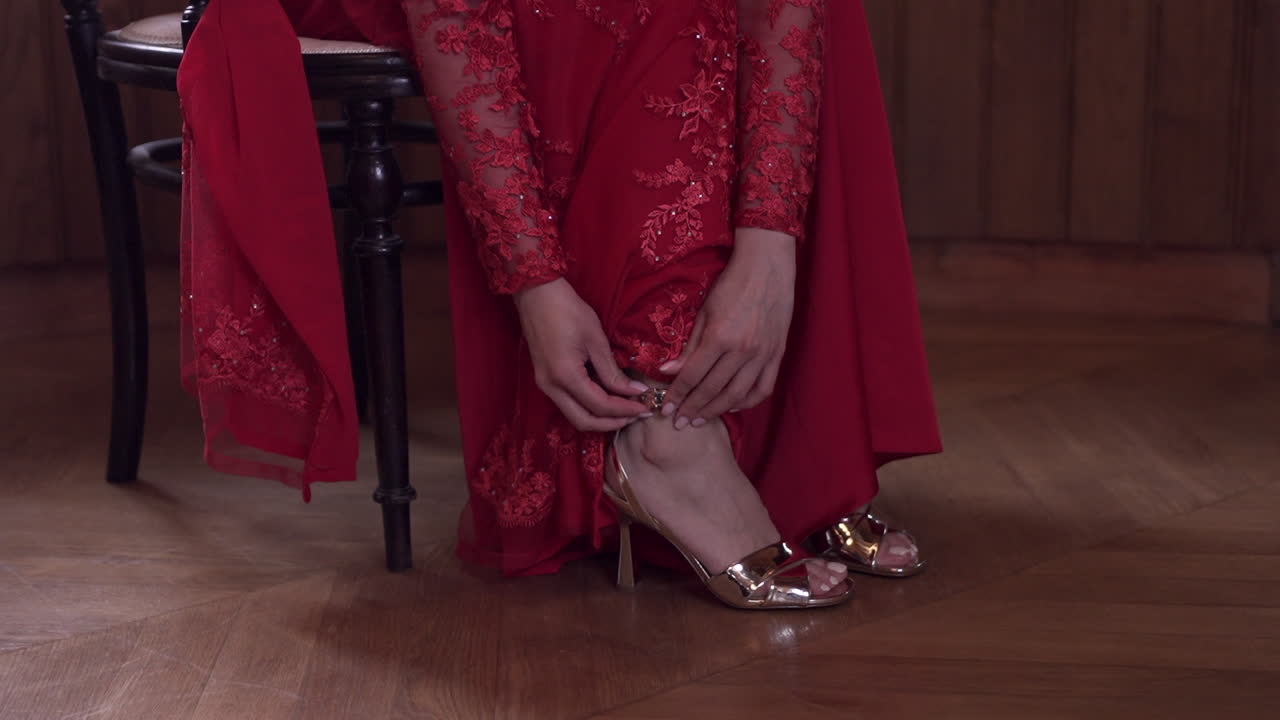 mujer en elegante vestido de encaje rojo ajustando sus tacones altos dorados, preparándose para un evento