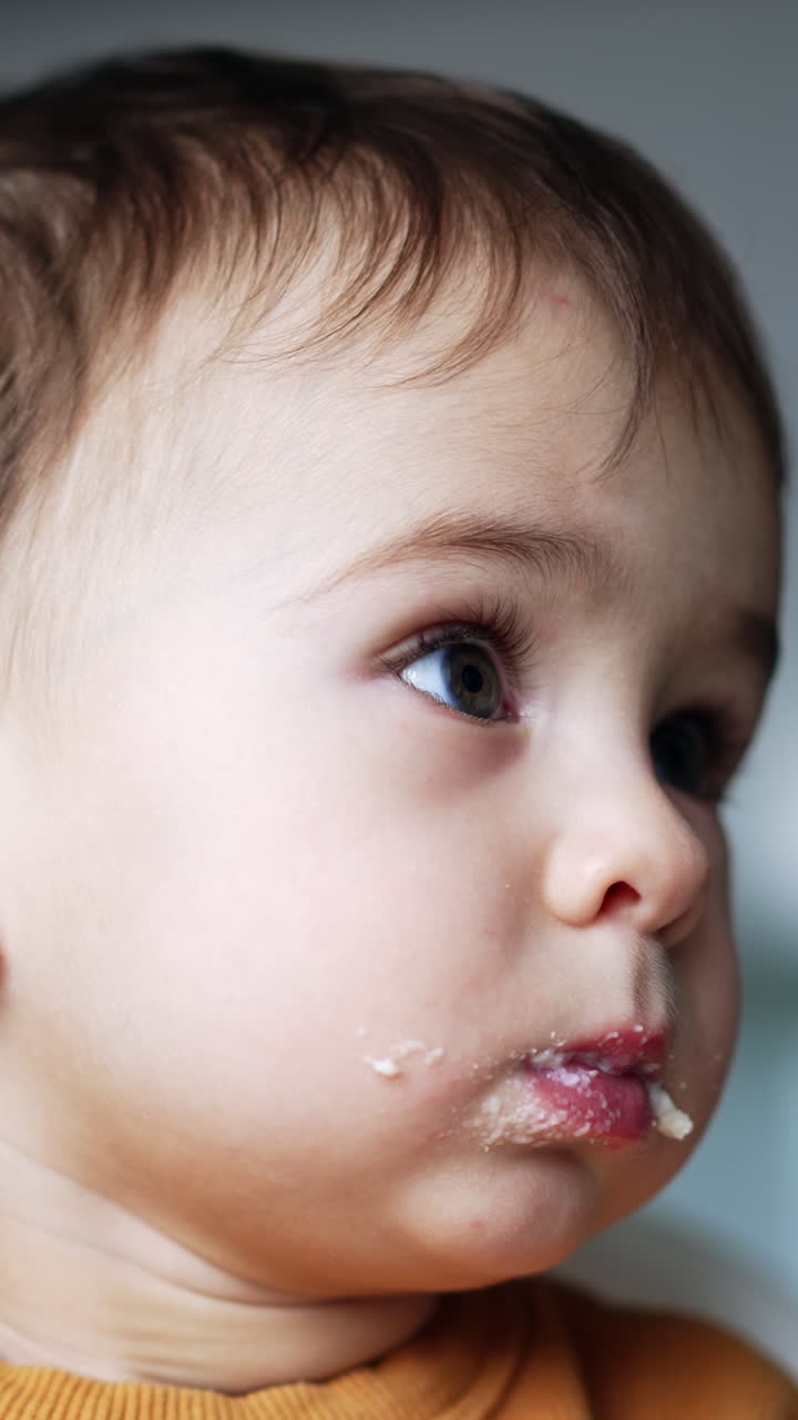Beautiful Caucasian baby boy with food around his mouth. Mom gives the spoon with dairy to her son. Low angle view. Vertical video