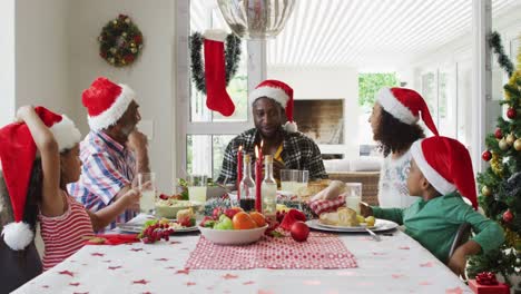 Fröhliche-Afroamerikanische-Familie-Mit-Mehreren-Generationen,-Die-Weihnachtsmützen-Trägt-Und-Das-Feiertagsessen-Feiert