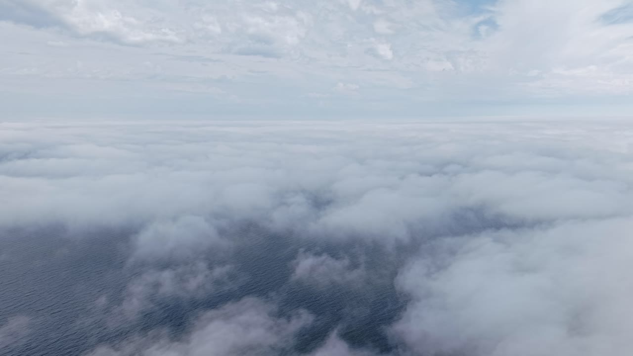 Aerial over sea of clouds, smooth layered mist floating beneath soft blue sky