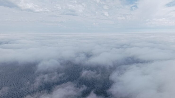 Luftfoto over et skyhav, hvor blød, lagdelt tåge svæver under en mild blå himmel.